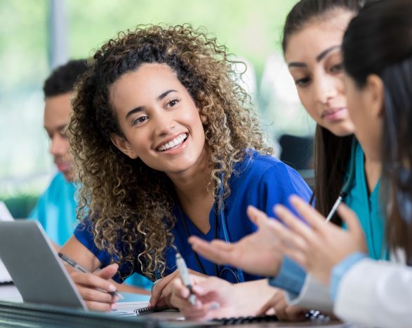 A diverse group of nurses talking in front of a laptop computer.