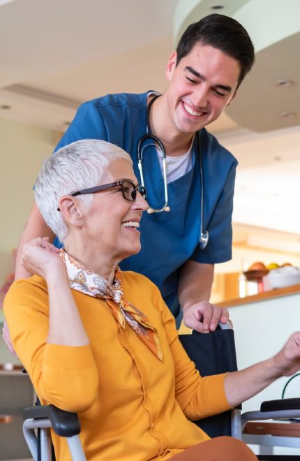 A male nurse stands behind a female patient in a wheelchair.